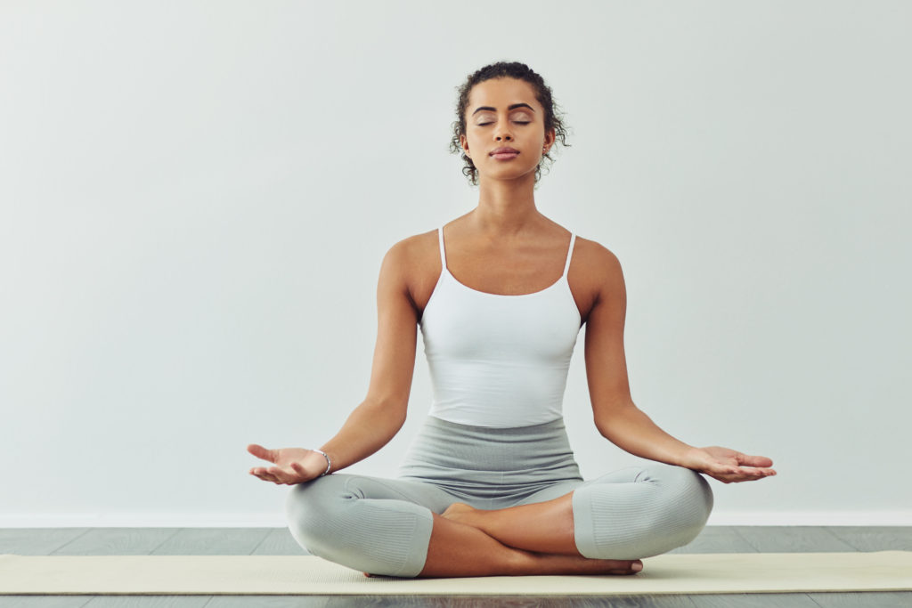woman meditating on a yoga mat against a grey background
