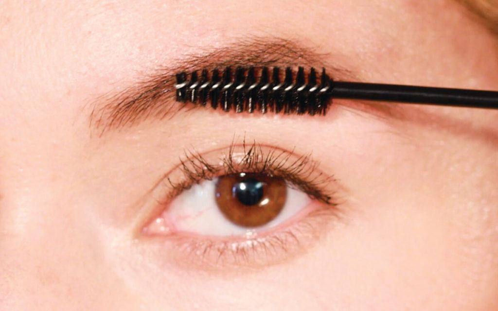 brushing serum through eyebrows with a spoolie brush